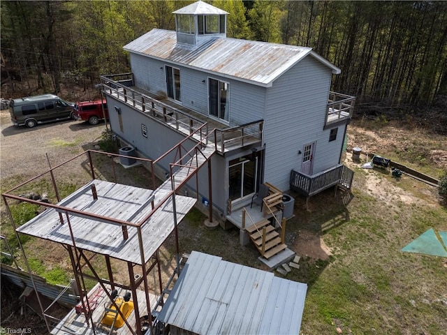 rear view of property featuring a balcony, a view of trees, a deck, and stairs