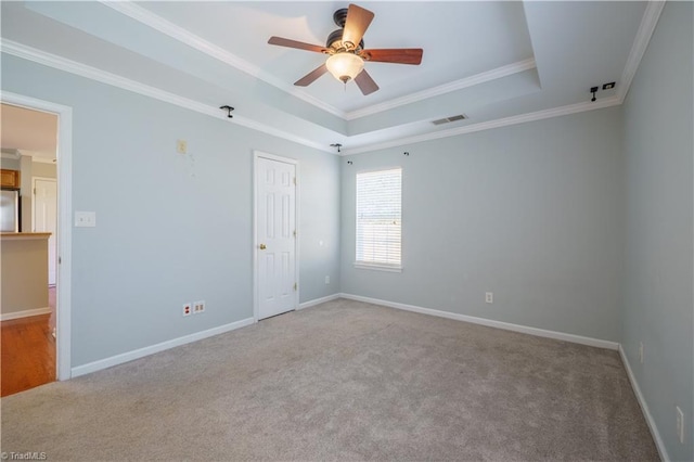 carpeted empty room featuring baseboards, a tray ceiling, visible vents, and crown molding