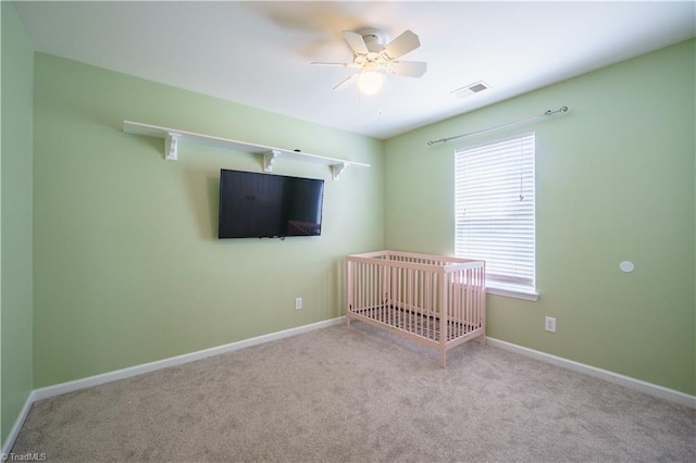 unfurnished bedroom with a ceiling fan, visible vents, baseboards, a crib, and carpet