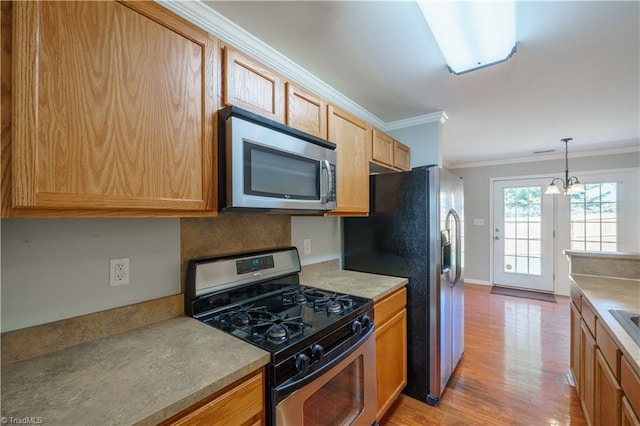 kitchen featuring crown molding, stainless steel appliances, light wood-type flooring, an inviting chandelier, and pendant lighting