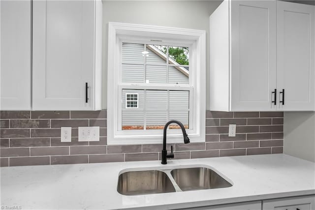 kitchen with light stone countertops, white cabinetry, sink, and tasteful backsplash