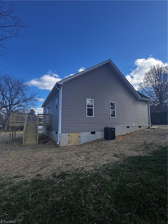 view of side of home with a deck, a yard, and central air condition unit