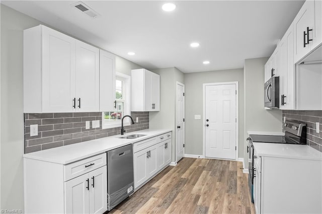 kitchen featuring appliances with stainless steel finishes, light wood-type flooring, tasteful backsplash, sink, and white cabinets