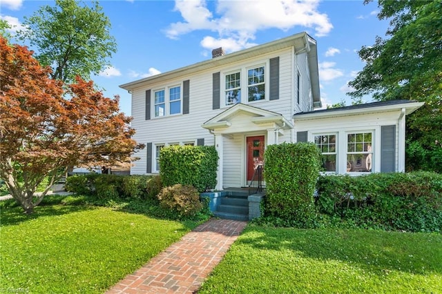 colonial inspired home featuring a chimney and a front yard