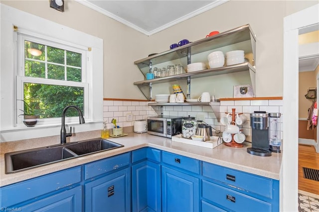 kitchen featuring tasteful backsplash, a sink, crown molding, stainless steel microwave, and blue cabinets