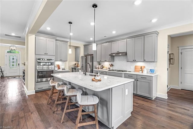 7733 Michaelis St, Greensboro, NC 27455 - kitchen featuring gray cabinetry, appliances with stainless steel finishes, under cabinet range hood, decorative backsplash, and a breakfast bar