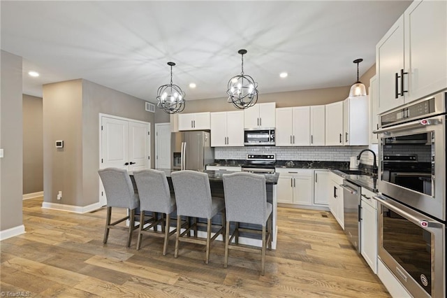 kitchen featuring decorative backsplash, appliances with stainless steel finishes, white cabinets, a sink, and a kitchen breakfast bar