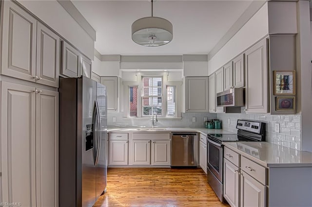 kitchen with tasteful backsplash, gray cabinetry, sink, light wood-type flooring, and stainless steel appliances