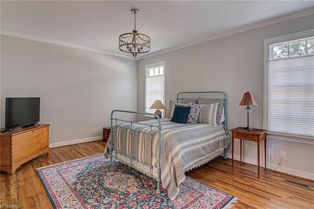 bedroom with an inviting chandelier, multiple windows, ornamental molding, and light wood-type flooring