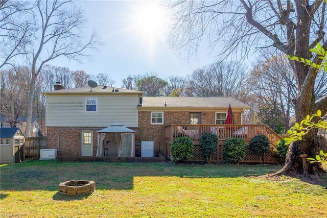 rear view of property with a storage unit, a deck, an outdoor fire pit, and a yard