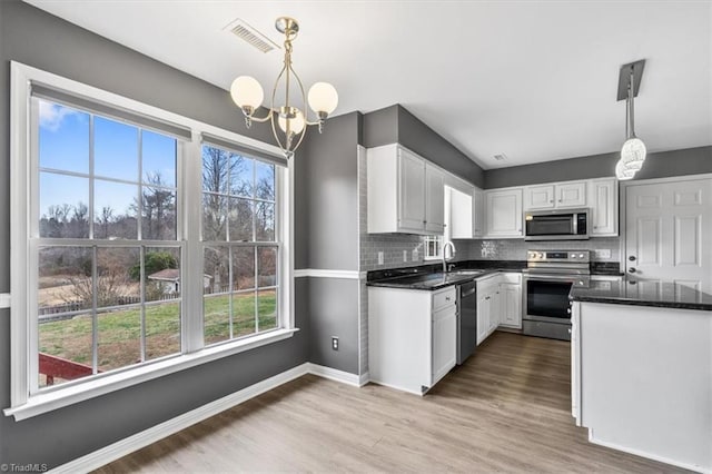 kitchen with stainless steel appliances, sink, white cabinets, a chandelier, and pendant lighting