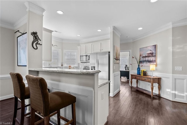 kitchen featuring crown molding, appliances with stainless steel finishes, white cabinetry, dark hardwood / wood-style flooring, and kitchen peninsula