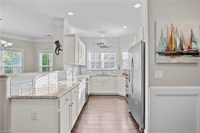 kitchen with decorative backsplash, kitchen peninsula, light stone counters, sink, and white cabinets