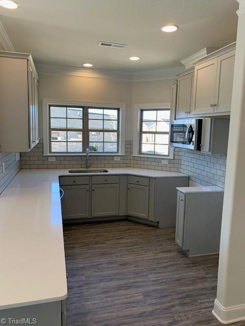 kitchen with sink, backsplash, dark hardwood / wood-style floors, gray cabinetry, and crown molding