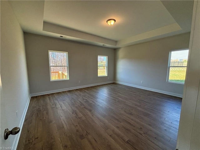 empty room featuring a raised ceiling, baseboards, and dark wood-style flooring