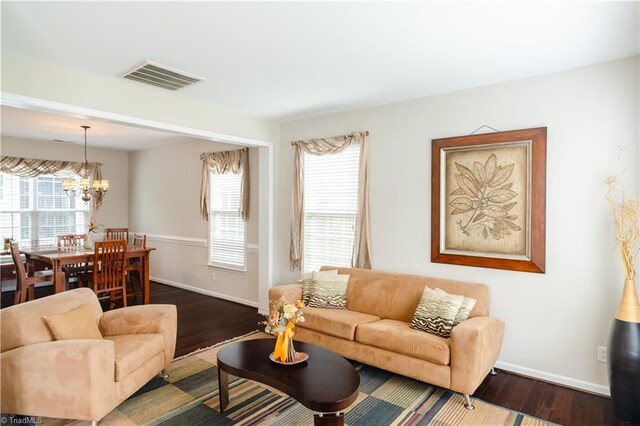 living room featuring an inviting chandelier, a healthy amount of sunlight, and dark hardwood / wood-style flooring