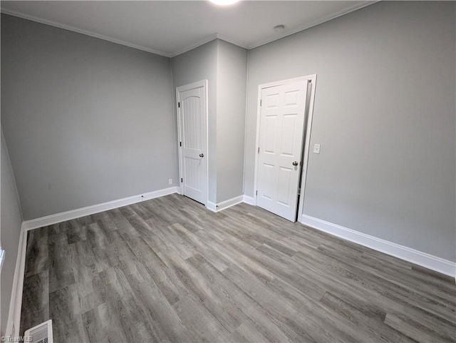 empty room with ornamental molding, wood finished floors, visible vents, and baseboards