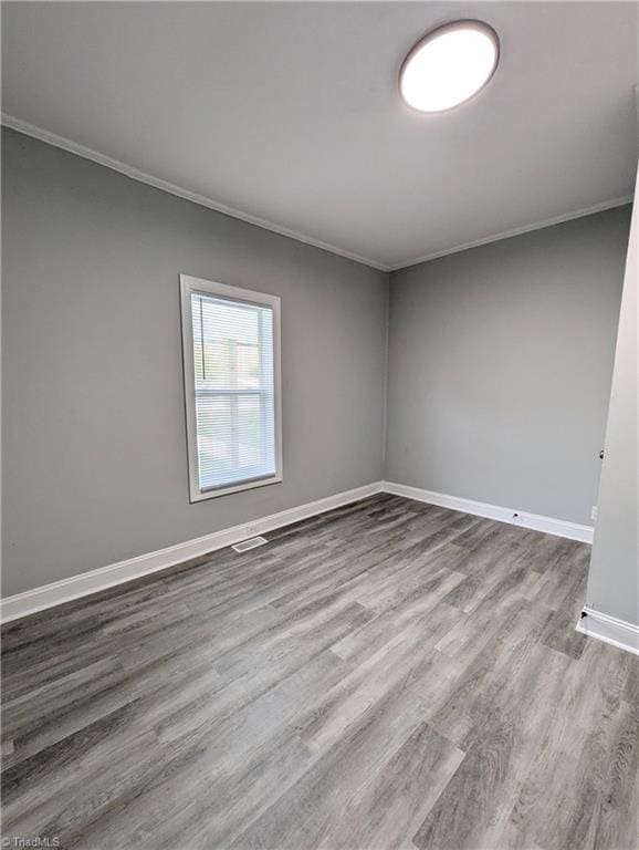 unfurnished room with baseboards, visible vents, ornamental molding, and wood finished floors