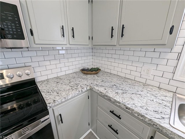 kitchen with light stone counters, a sink, stainless steel electric range oven, and decorative backsplash