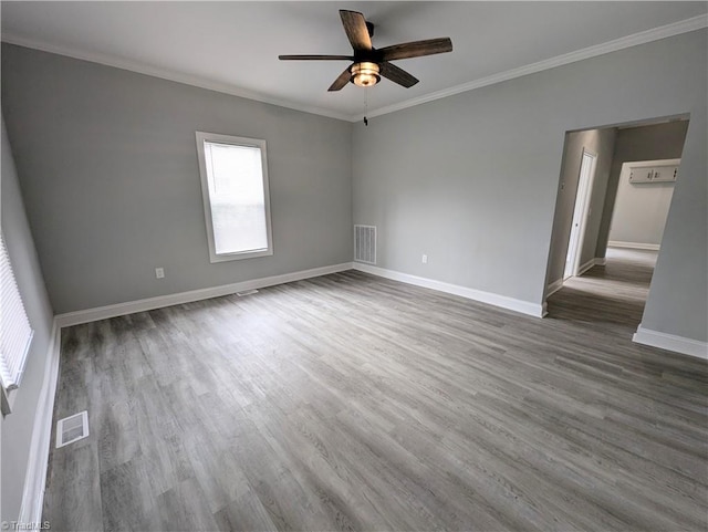 empty room with ornamental molding, wood finished floors, visible vents, and baseboards