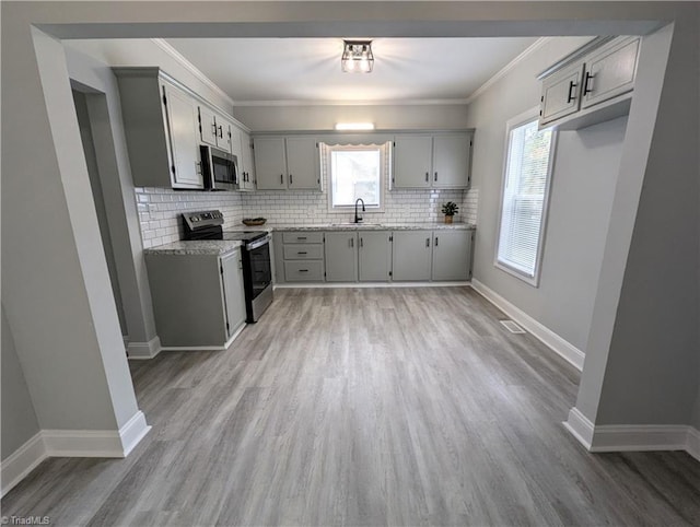 kitchen with light wood-style flooring, gray cabinetry, stainless steel appliances, a sink, and backsplash