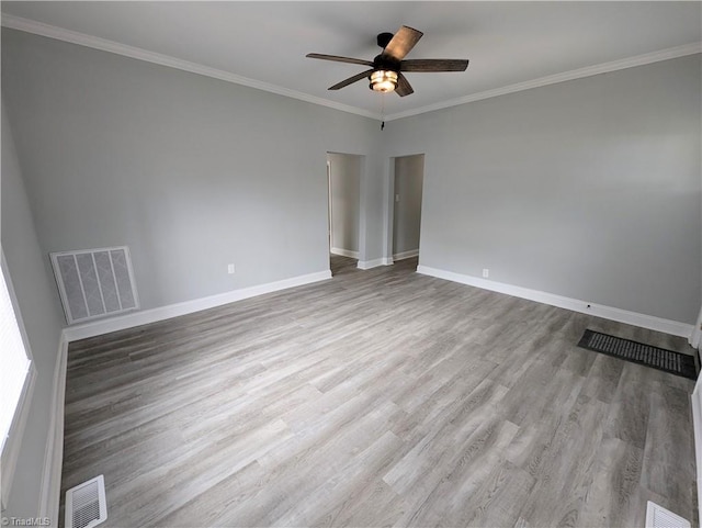 empty room with ornamental molding, visible vents, baseboards, and wood finished floors