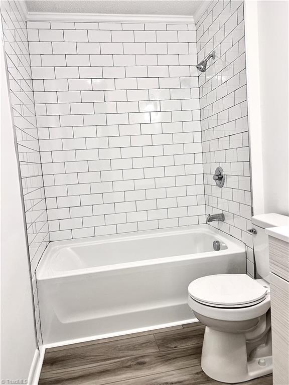 full bathroom featuring crown molding, tiled shower / bath combo, vanity, wood-type flooring, and toilet