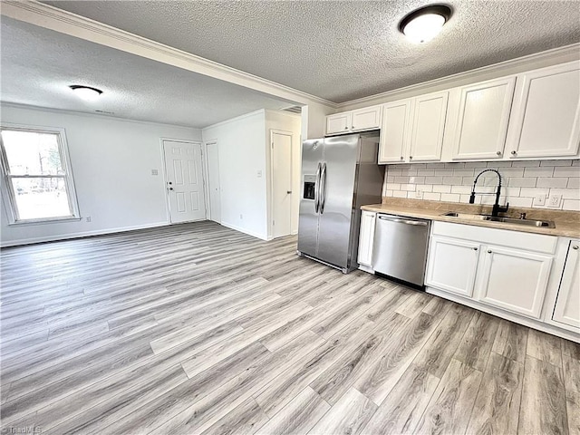 kitchen with appliances with stainless steel finishes, sink, backsplash, white cabinets, and light wood-type flooring