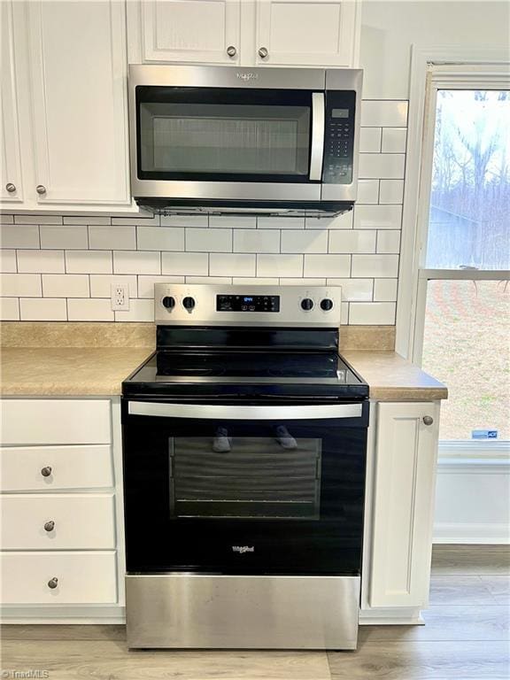 kitchen featuring tasteful backsplash, stainless steel appliances, white cabinets, and light wood-type flooring