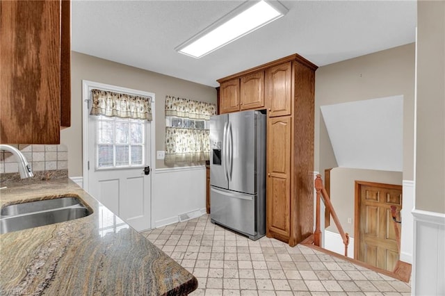 kitchen featuring stainless steel fridge with ice dispenser, sink, and dark stone counters