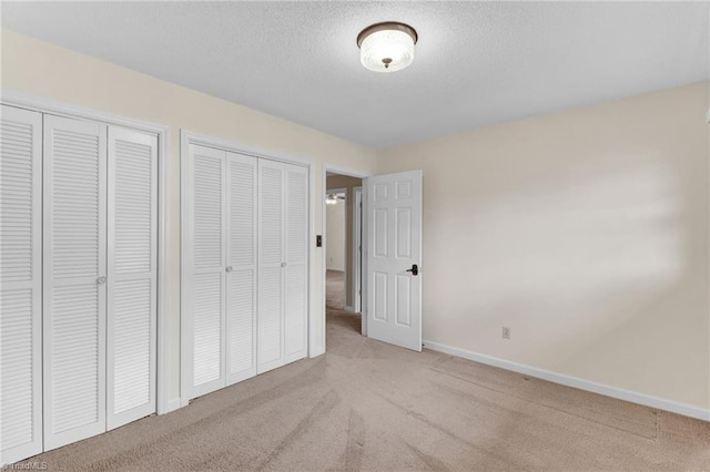 unfurnished bedroom featuring light colored carpet, a textured ceiling, and two closets