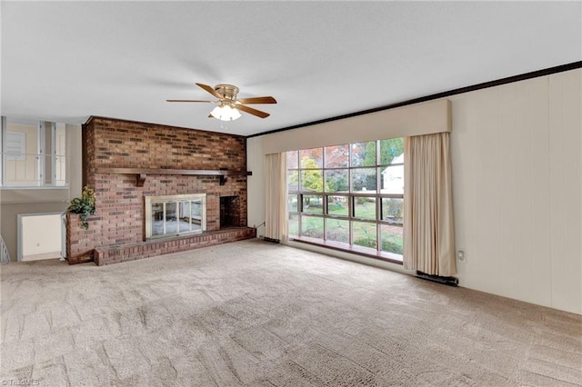 unfurnished living room featuring ceiling fan, carpet floors, a fireplace, and ornamental molding