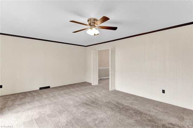 spare room with light colored carpet, ceiling fan, ornamental molding, and wood walls