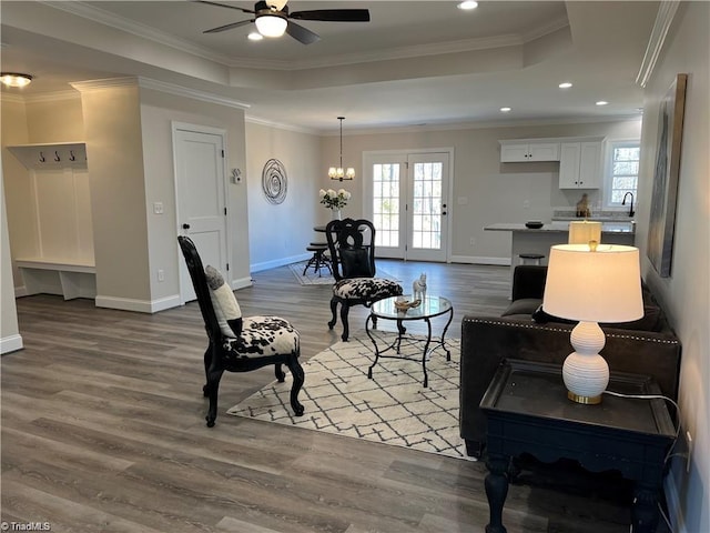 living room with french doors, ceiling fan with notable chandelier, crown molding, a raised ceiling, and light wood-type flooring