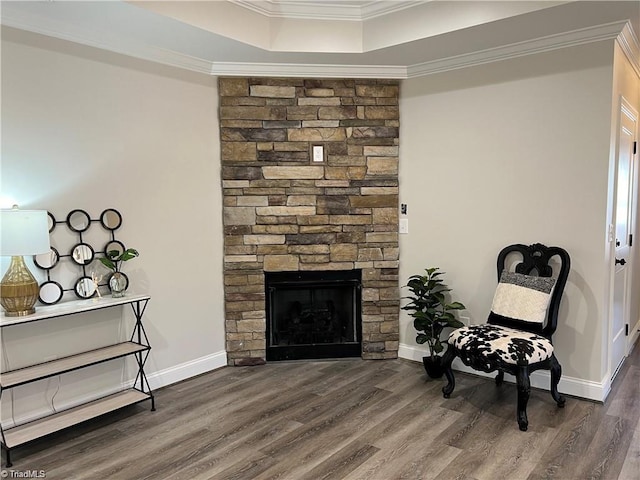 sitting room with crown molding, dark hardwood / wood-style floors, a raised ceiling, and a stone fireplace