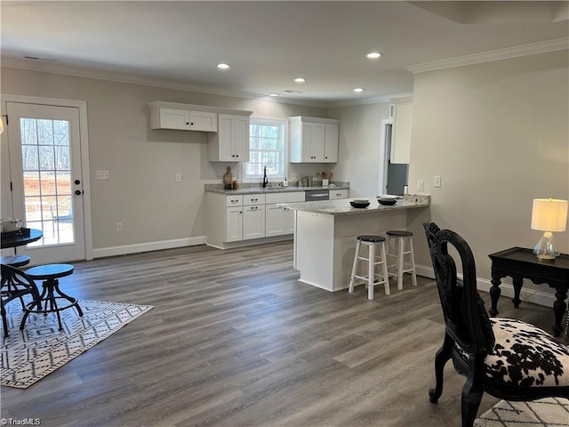 kitchen featuring kitchen peninsula, stainless steel dishwasher, a kitchen bar, white cabinetry, and hardwood / wood-style flooring