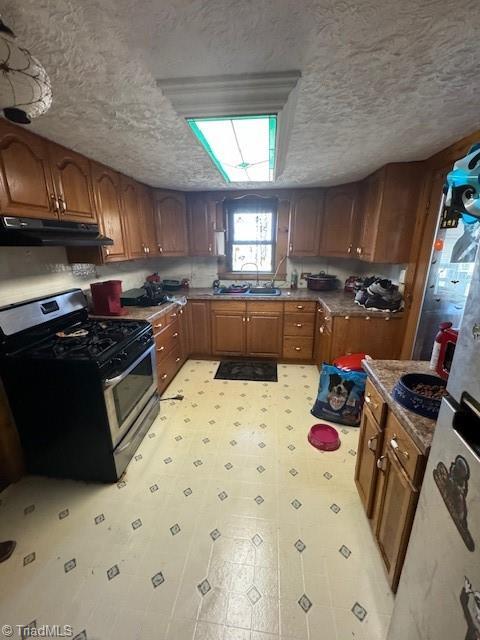 kitchen with stainless steel range with gas cooktop, brown cabinets, light floors, light countertops, and under cabinet range hood