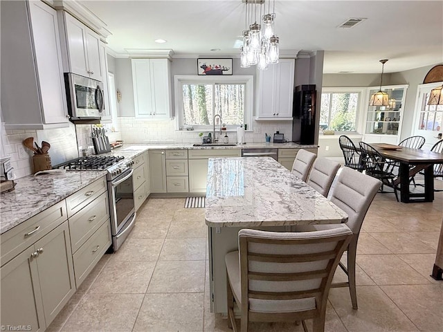 kitchen featuring a breakfast bar area, a kitchen island, a sink, appliances with stainless steel finishes, and pendant lighting