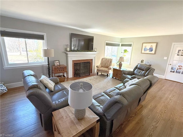 living room with a healthy amount of sunlight, a brick fireplace, baseboards, and wood finished floors