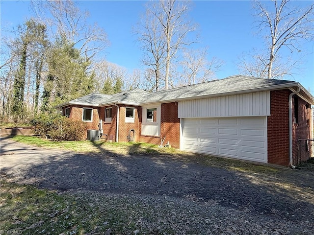 single story home with a garage, brick siding, driveway, and central AC unit