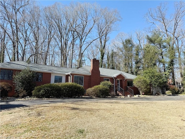 ranch-style home with a front yard, a chimney, and brick siding