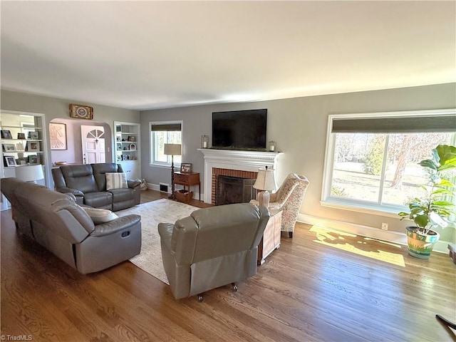 living area with a brick fireplace, visible vents, baseboards, and wood finished floors