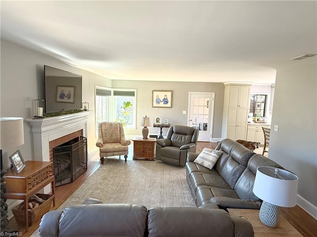 living area featuring baseboards, a brick fireplace, visible vents, and light wood-style floors