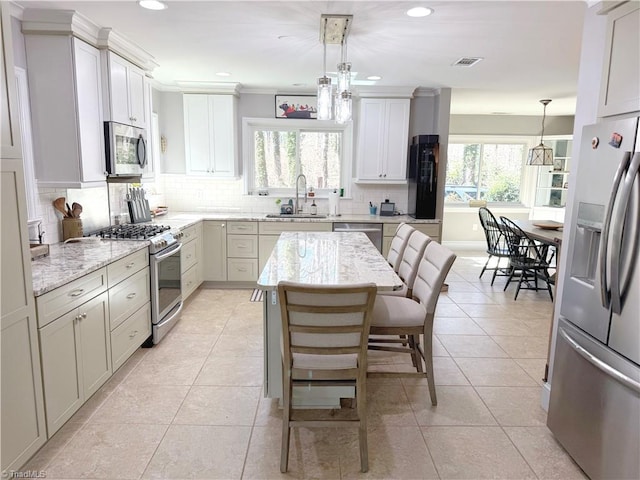 kitchen featuring light tile patterned floors, appliances with stainless steel finishes, light stone countertops, pendant lighting, and a sink