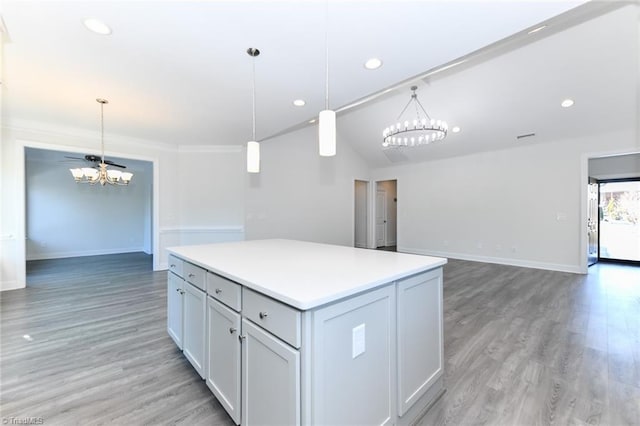 kitchen with hanging light fixtures, hardwood / wood-style floors, a kitchen island, an inviting chandelier, and crown molding