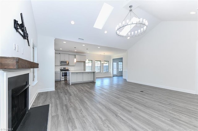 unfurnished living room with a skylight, high vaulted ceiling, a chandelier, and wood-type flooring