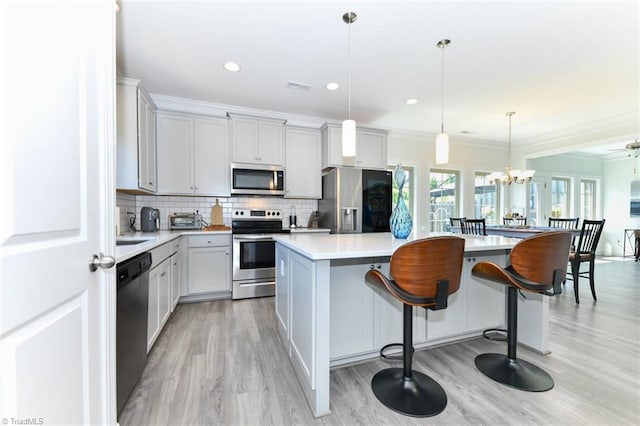 kitchen featuring a kitchen breakfast bar, light hardwood / wood-style floors, hanging light fixtures, a kitchen island, and appliances with stainless steel finishes