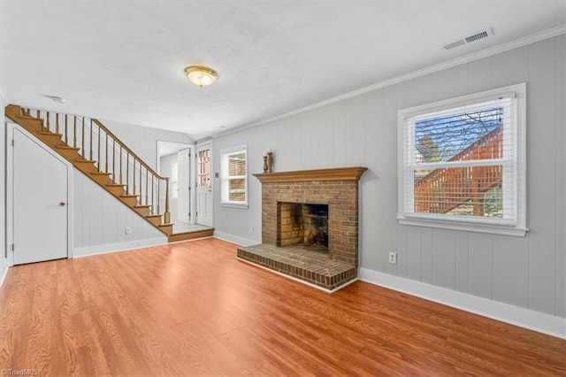 unfurnished living room featuring wood finished floors, visible vents, baseboards, stairs, and a brick fireplace