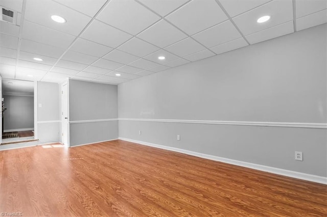 below grade area with visible vents, a drop ceiling, wood finished floors, recessed lighting, and baseboards