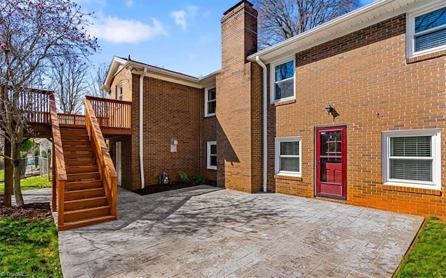 back of property featuring stairs, a wooden deck, brick siding, and a chimney